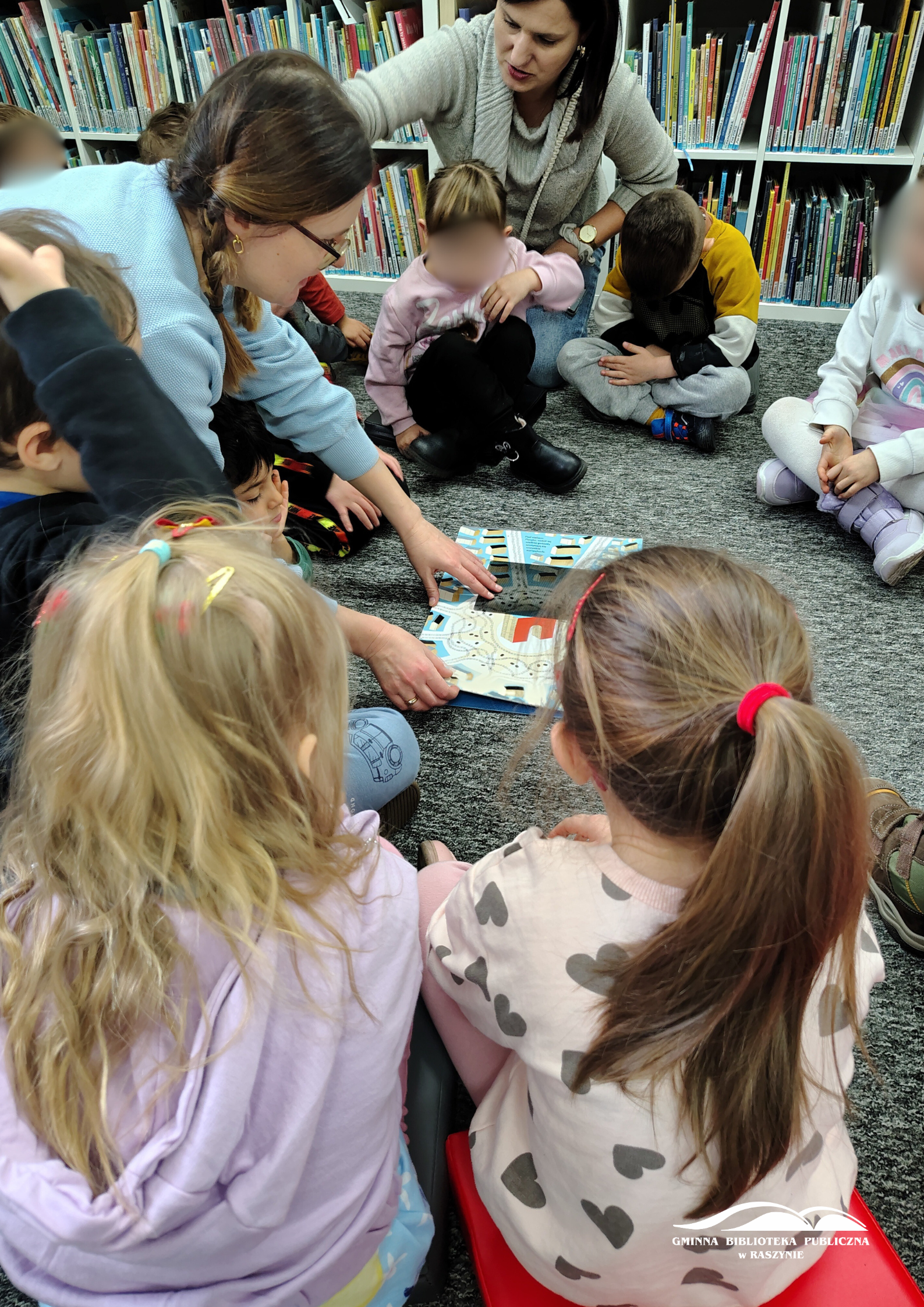 Bibliotekarka pokazuje ilustracje, dzieci siedzą dookoła i patrzą