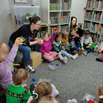 Dzieci siedzą w koło, pokazując konstrukcje z klocków Lego