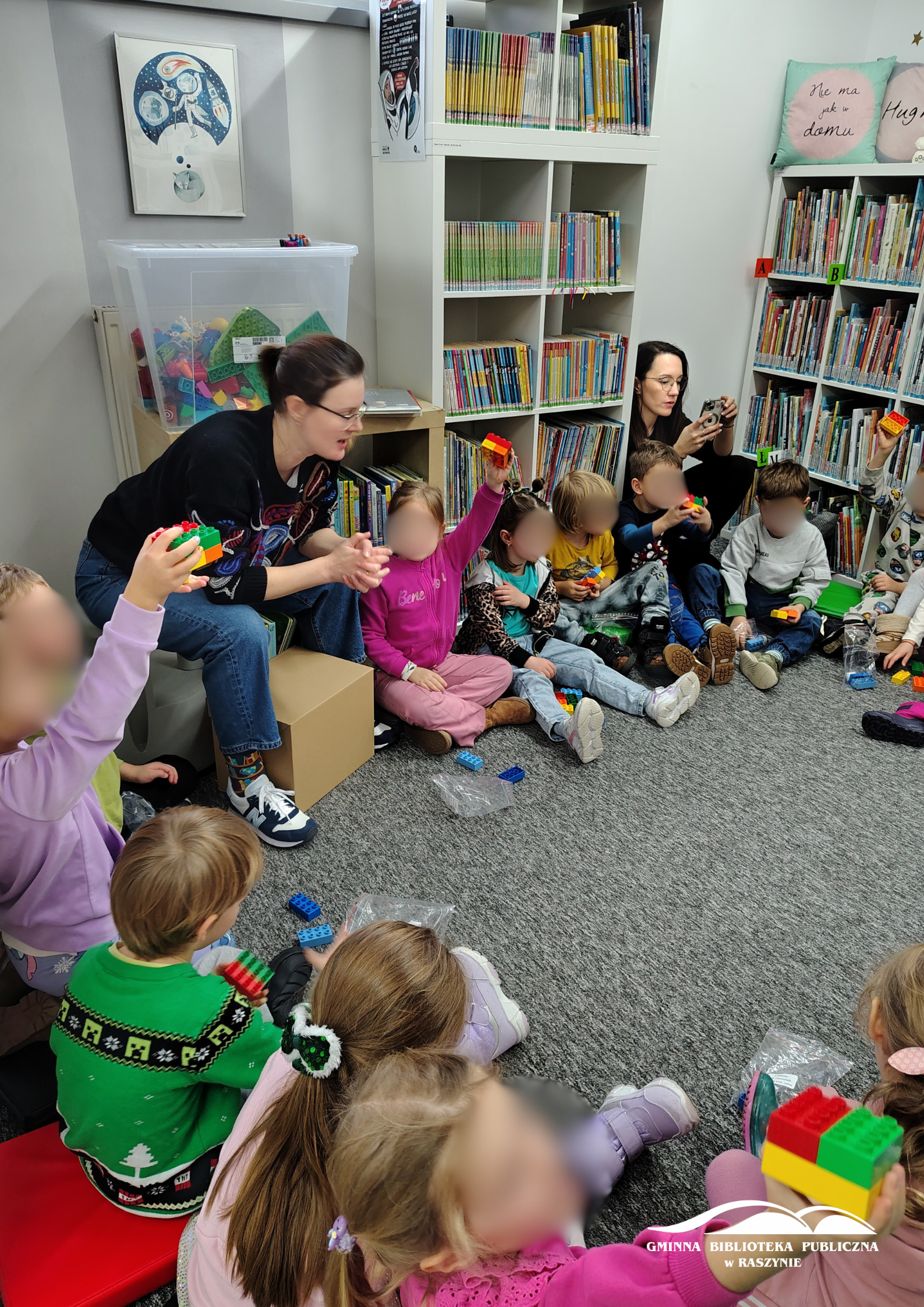 Dzieci siedzą w koło, pokazując konstrukcje z klocków Lego