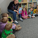 Dzieci siedzą w koło w dziale dla najmłodszych, bibliotekarka pokazuje książkę o Mikołaju