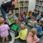 Bibliotekarka wysypuje klocki Lego z dużego pudła, dzieci siedzą na dywanie
