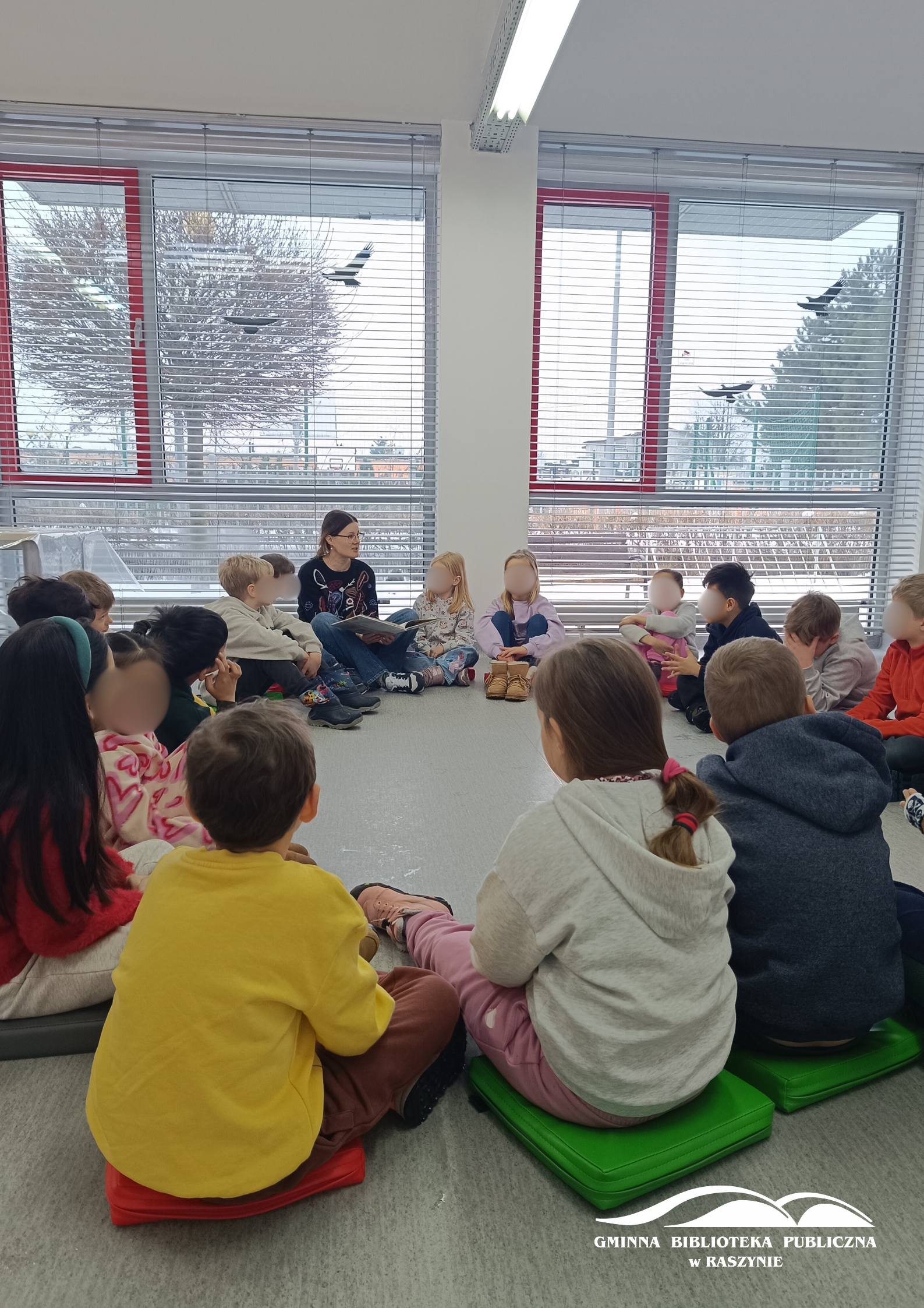 Dzieci siedzą w koło, bibliotekarka czyta książkę