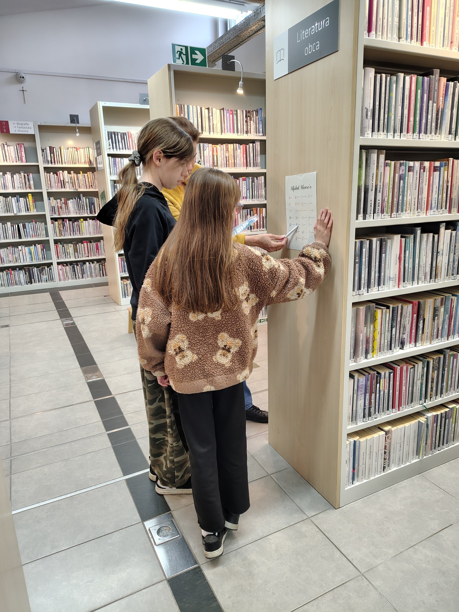 Grupa dziewczynek podczas odczytywania zagadki z regału bibliotecznego