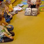 Bibliotekarka pokazuje książkę z obrazkami 3d, po lewej widoczne siedzące dzieci
