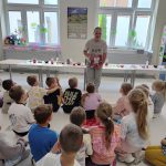 Bibliotekarka pokazuje książkę "Brud", uczniowie siedzą na podłodze