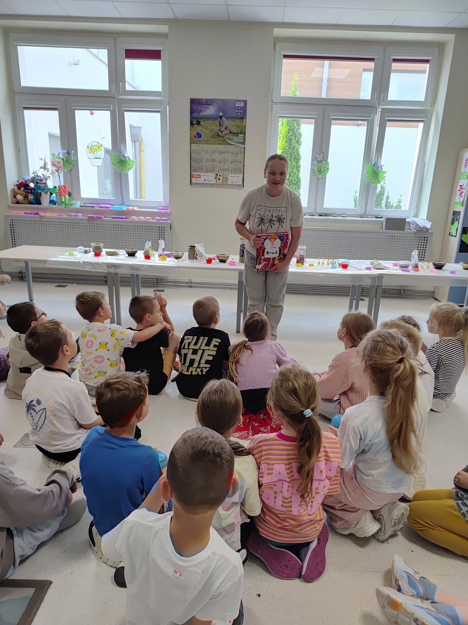 Bibliotekarka pokazuje książkę "Brud", uczniowie siedzą na podłodze