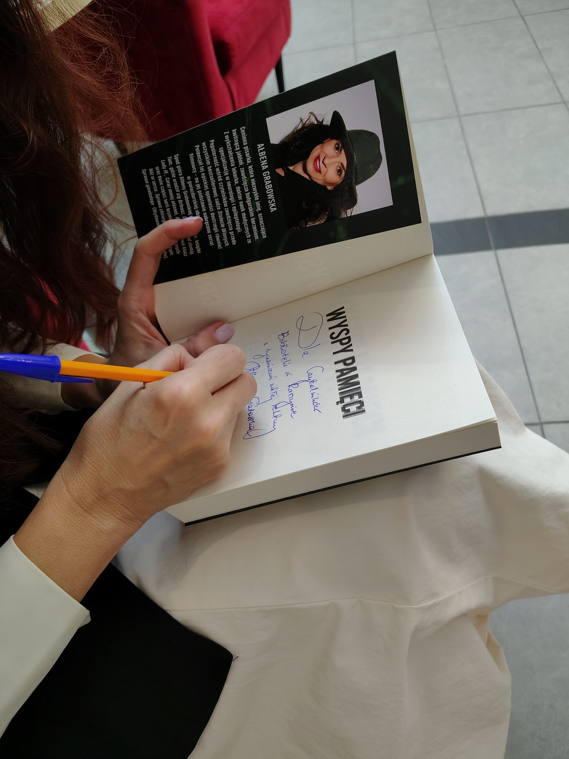 Zbliżenie na otwartą książkę z dedykacją, widoczna dłoń pisarki
